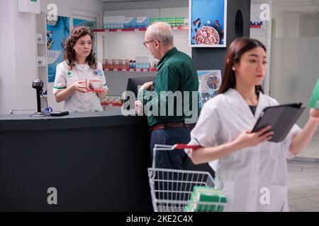 Homme senior parlant avec le caissier de la pharmacie pour demander des conseils médicaux pendant l'achat de médicaments dans la pharmacie. Le pharmacien recommande des pilules de cardiologie pour prévenir la maladie. Concept de médecine Banque D'Images