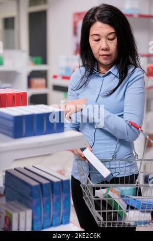 Femme asiatique mettant boîte de pilules dans le panier pour acheter des médicaments sur ordonnance et des produits médicaux. Client prenant des médicaments pharmaceutiques paquet pour guérir la maladie, les fournitures de santé capsules. Banque D'Images