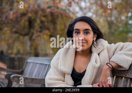 La jeune femme indienne sourit timidement à la caméra tout en étant assise sur un banc public. Banque D'Images