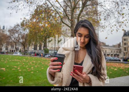 Une fille indienne aux cheveux longs tout en marchant dans les messages du parc et en boit du thé chaud. Banque D'Images