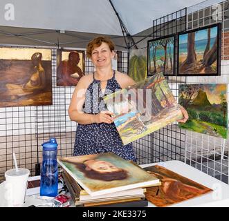 Honolulu, Hawaii, 8 octobre 2022 - Chinatown Street art show - Woman montre l'un de ses tableaux dans un stand entouré par son travail. Banque D'Images