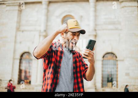 Un fan de football réagit avec enthousiasme à un match de football en regardant son téléphone portable. Concept de personnes et de sports. Banque D'Images