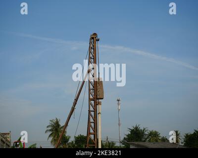 Le pieu de béton est conduit dans le sol sur le chantier de construction à l'aide d'une machine à pieux avec ciel bleu et nuage blanc en arrière-plan Banque D'Images