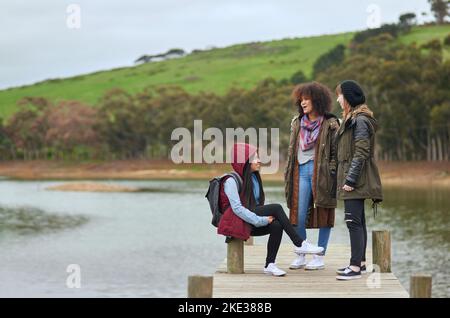 Sœurs au coeur. Un groupe d'amis ayant une conversation sur un quai au bord d'un lac. Banque D'Images