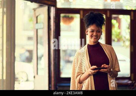 wifi gratuit est toujours un plus. Portrait d'une jeune femme attirante qui envoie des SMS sur son téléphone portable dans un café. Banque D'Images