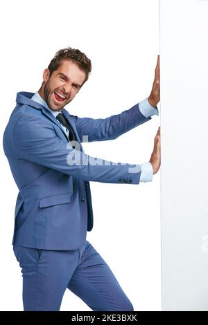 Défiez vos limites. Photo studio d'un homme d'affaires charmant poussant un mur contre un fond blanc. Banque D'Images