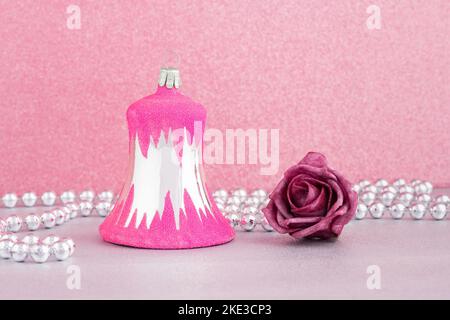 Une boule de noël rose vintage en forme de cloche avec une guirlande argentée ornée de perles et une rose pourpre sur fond rose. Banque D'Images
