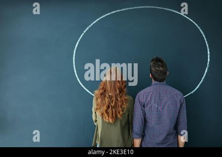 Que voyez-vous ? Photo d'un jeune couple regardant un cercle vide dessiné sur un tableau noir. Banque D'Images