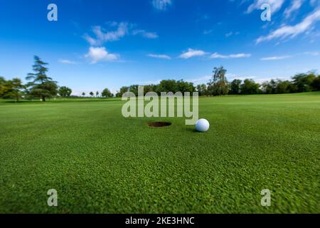 Ballon blanc placé sur l'herbe verte près du trou dans le sol contre ciel bleu nuageux pendant le match de golf Banque D'Images