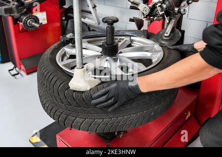 De dessus récolte homme ouvrier de garage en gants de démontage du pneu de la jante à l'aide de machines spéciales Banque D'Images