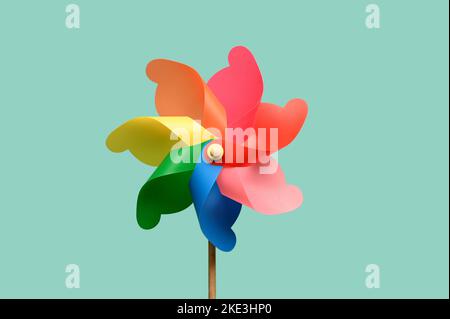 Roue à pincettes en papier brillant avec boucles multicolores sur un bâton fin isolé sur fond bleu clair Banque D'Images