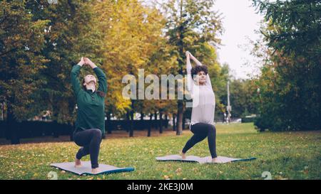 La jeune fille mince élève de yoga apprend Eagle pose sous la direction d'un enseignant expérimenté pendant la pratique individuelle avec un instructeur dans le parc. Belle nature d'automne est en arrière-plan. Banque D'Images