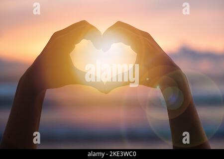 Mains formant un coeur avec silhouette de coucher de soleil Banque D'Images