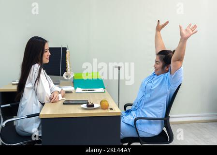 Une femme d'Asie en surpoids a soulevé la main et a discuté des résultats des tests avec une femme médecin à l'hôpital, concept d'épaule gelée. Banque D'Images