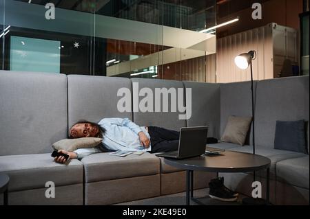 Zombie surtravaillé dormant sur le canapé dans le bureau Banque D'Images