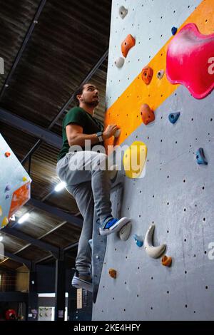 Un beau grimpeur de rochers qui monte sur des pentes colorées sur le mur d'escalade de la salle de gym Banque D'Images