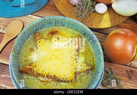 Gros plan d'un bol bleu isolé avec soupe à l'oignon, pain grillé gratiné et fromage pecorino parmesan râpé, thym, ail, oignons ingrédients sur le bois t. Banque D'Images