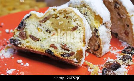 Gros plan de christstollen tranché isolé avec des raisins secs, du sucre blanc en poudre et du massepain sur la plaque rouge Banque D'Images