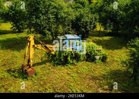 Un vieux tracteur avec un godet, abandonné d'un jardin vert Banque D'Images