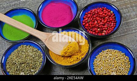 Vue de dessus sur six bols isolés bleus avec diverses épices saines colorées, poudre et condiments de grain sur table en bois. Verser dans un bol curcuma curcuma curcuma. Banque D'Images