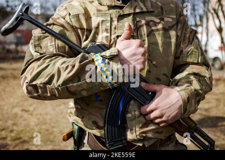 L'homme en camouflage avec un bracelet en ruban jaune et bleu sur sa main tenant le fusil automatique Kalashnikov Banque D'Images