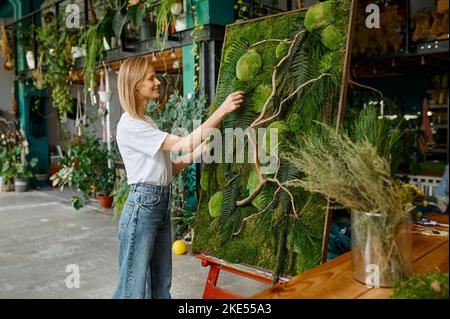 Jeune fleuriste heureux décorateur créant panneau de mousse de plante Banque D'Images