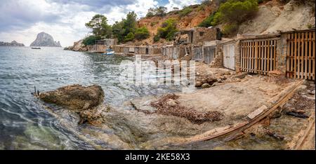 La plage à es Vedra avec des garages pour bateaux et un ciel nuageux en arrière-plan, l'Espagne Banque D'Images