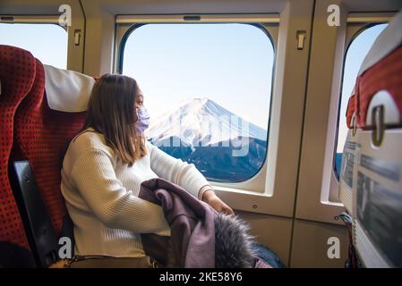 Yong femme asiatique portant un masque et tenant une veste assise dans le train à grande vitesse lors d'un voyage au Japon. Banque D'Images