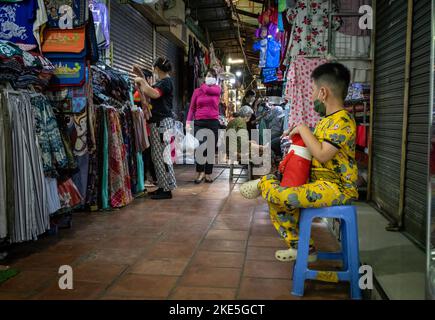 Un jeune garçon vêtu de pyjamas jaunes est assis sur un tabouret dans une ruelle du marché russe de Phnom Penh, au Cambodge. Banque D'Images