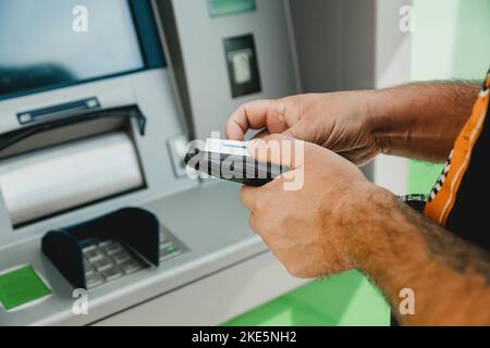 Carte ATM MAN. Carte d'insertion ATM. Homme mettant la carte de crédit dans le distributeur automatique de billets tout en tenant le portefeuille Banque D'Images