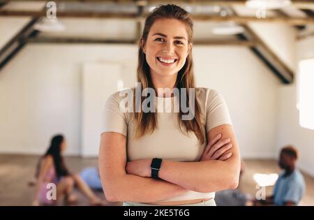 Portrait d'une jeune femme sportive souriant à l'appareil photo tout en se tenant dans un cours de fitness avec ses bras croisés. Bonne jeune femme ayant un exercice s Banque D'Images