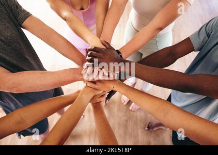 Vue de dessus d'un groupe de personnes multiculturelles mettant leurs mains ensemble dans un caucus avant le yoga. Groupe de jeunes sportifs commençant un cours de yoga i Banque D'Images