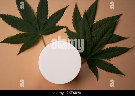 Une maquette pour votre produit cosmétique de soin du visage et du corps à base de cannabis médical. Crème sur fond marron clair. Copier l'espace. Pose à plat. Concept de santé et de bien-être. Banque D'Images