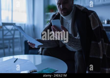 homme figé avec des factures regardant le smartphone près de l'argent sur la table au crépuscule Banque D'Images