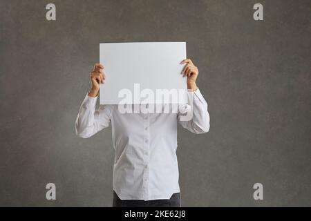 Man tient une feuille blanche de papier vierge devant son visage, espace de copie. Banque D'Images