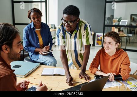 Groupe de jeunes designers interculturels heureux préparant la présentation d'un nouveau projet ou discutant d'idées et de stratégies lors d'une réunion Banque D'Images