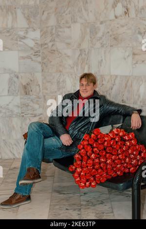 beau homme avec un énorme bouquet de roses scarlet est assis dans la salle d'attente. Un homme heureux félicite sa femme pour la naissance d'un enfant, un mercredi Banque D'Images