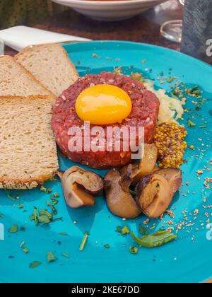 Filet de bœuf cru au tartre gastronomique avec jaune d'œuf et boletus marinés pour un gros plan sur une assiette moderne Banque D'Images