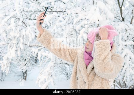 jeune femme sur le fond d'une belle plante dans la neige. Une jeune femme prend un selfie et rit en miriant lors d'une chute de neige. Bonne humeur, joie, plaisir Banque D'Images