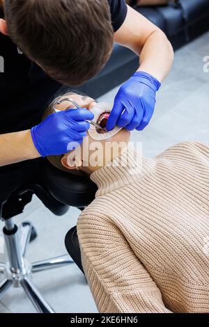 Les dents d'une femme avec des bretelles métalliques sont traitées à la clinique. Un orthodontiste utilise des instruments dentaires pour placer des bretelles sur les dents d'un patient. Sélection Banque D'Images