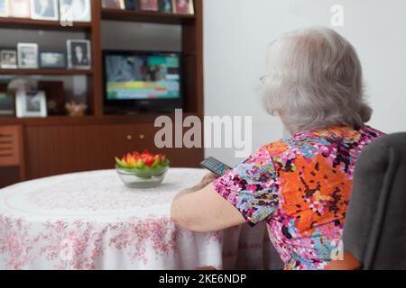 Femme âgée aux cheveux blancs regardant la télévision dans son salon, solitude des personnes âgées, connectivité avec le monde extérieur. Banque D'Images