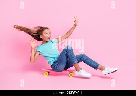 Photo pleine longueur de joli impressionné petit enfant porter t-shirt turquoise équitation skateboard recherche vide espace isolé couleur rose arrière-plan Banque D'Images