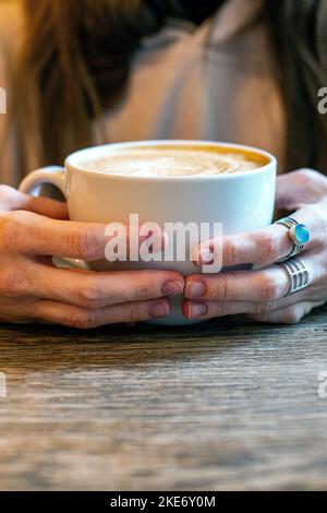 Les femmes tiennent les tasses à café Cappuccino sur fond de table rustique en bois Banque D'Images