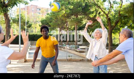 Club social de joyeux personnes âgées diverses appréciant le volley-ball le jour ensoleillé d'octobre plein air Banque D'Images