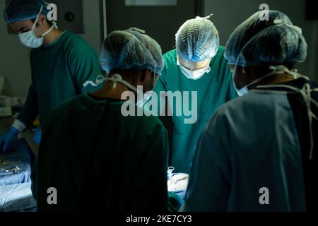 Divers groupes de chirurgiens féminins et masculins opérant sur des patients dans le bloc opératoire Banque D'Images