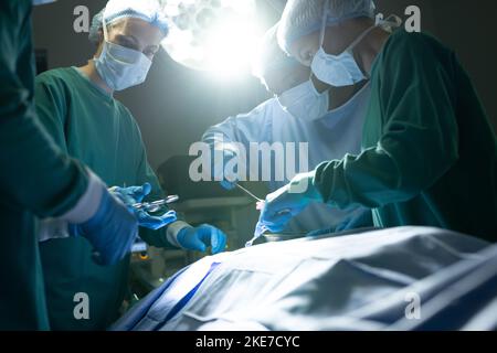 Divers groupes de chirurgiens féminins et masculins opérant sur des patients dans le bloc opératoire Banque D'Images