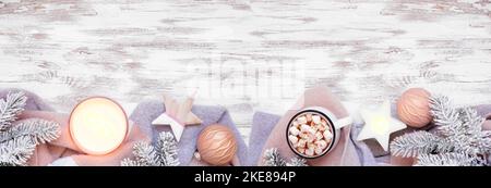 Bordure de Noël ou d'hiver confortable avec chandail gris et rose poussiéreux, bougie, chocolat chaud, branches enneigées et décor. Vue de haut en bas sur un rustique Banque D'Images