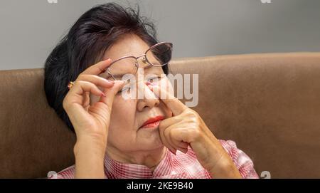 Femme asiatique âgée qui prend des lunettes, souffrant du syndrome des yeux secs Banque D'Images