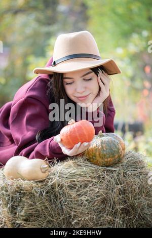 Jeune fille caucasienne assise dans le parc d'automne. Elle tient la citrouille orange dans ses mains. Saison d'automne Banque D'Images