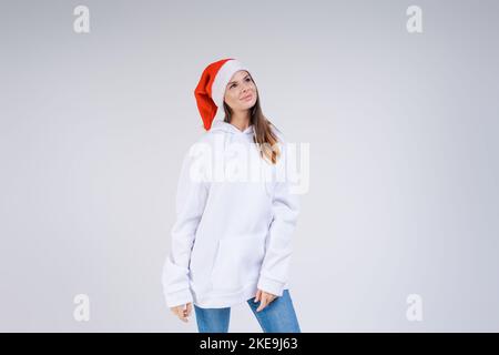 Portrait joyeuse jolie femme dans un chapeau rouge du Père Noël rit, en arrière-plan dans le studio. Belle fille semble heureuse et excitée. Joyeux Noël et bonne année pleine de plaisir. Banque D'Images